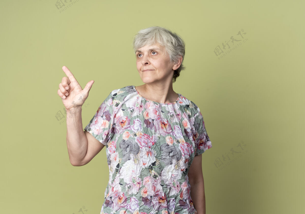橄榄色高兴的老妇人指着旁边的橄榄绿墙上孤零零的仰望向上老的女士