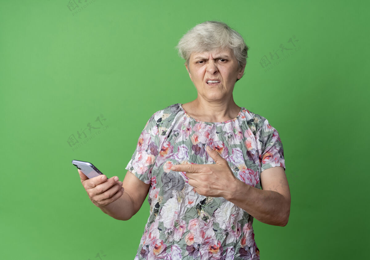 电话恼怒的老妇人拿着电话指着绿墙上的电话烦绿抱