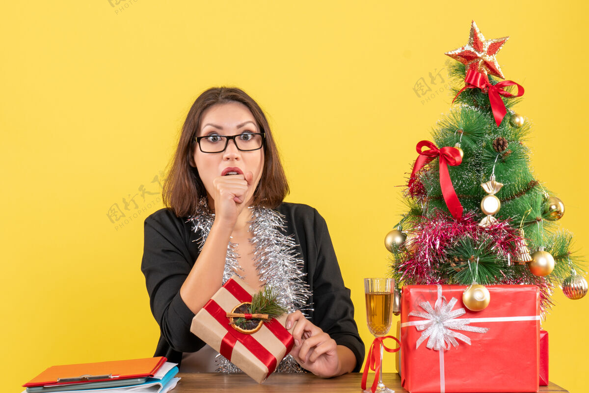 黄色新年的气氛 美丽的商务女士穿着西装 戴着眼镜 坐在办公室的桌子旁展示她的惊喜惊喜人套装