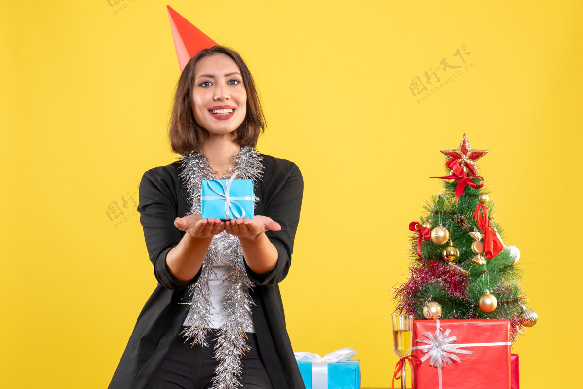 快乐圣诞心情积极美丽的女士拿着礼物高兴地在黄色的办公室时尚黑发成人