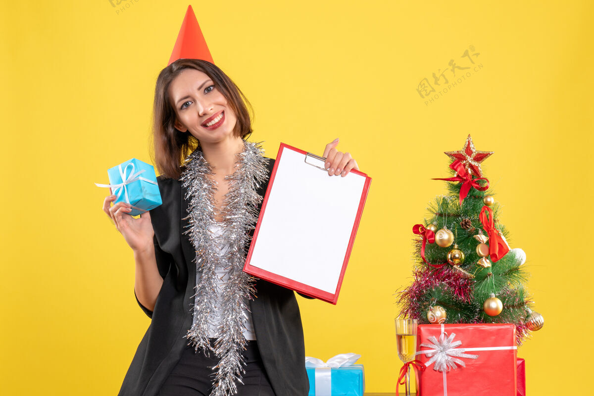 黄色圣诞气氛与美丽的女士举行文件和礼物在黄色的办公室女士圣诞节成人