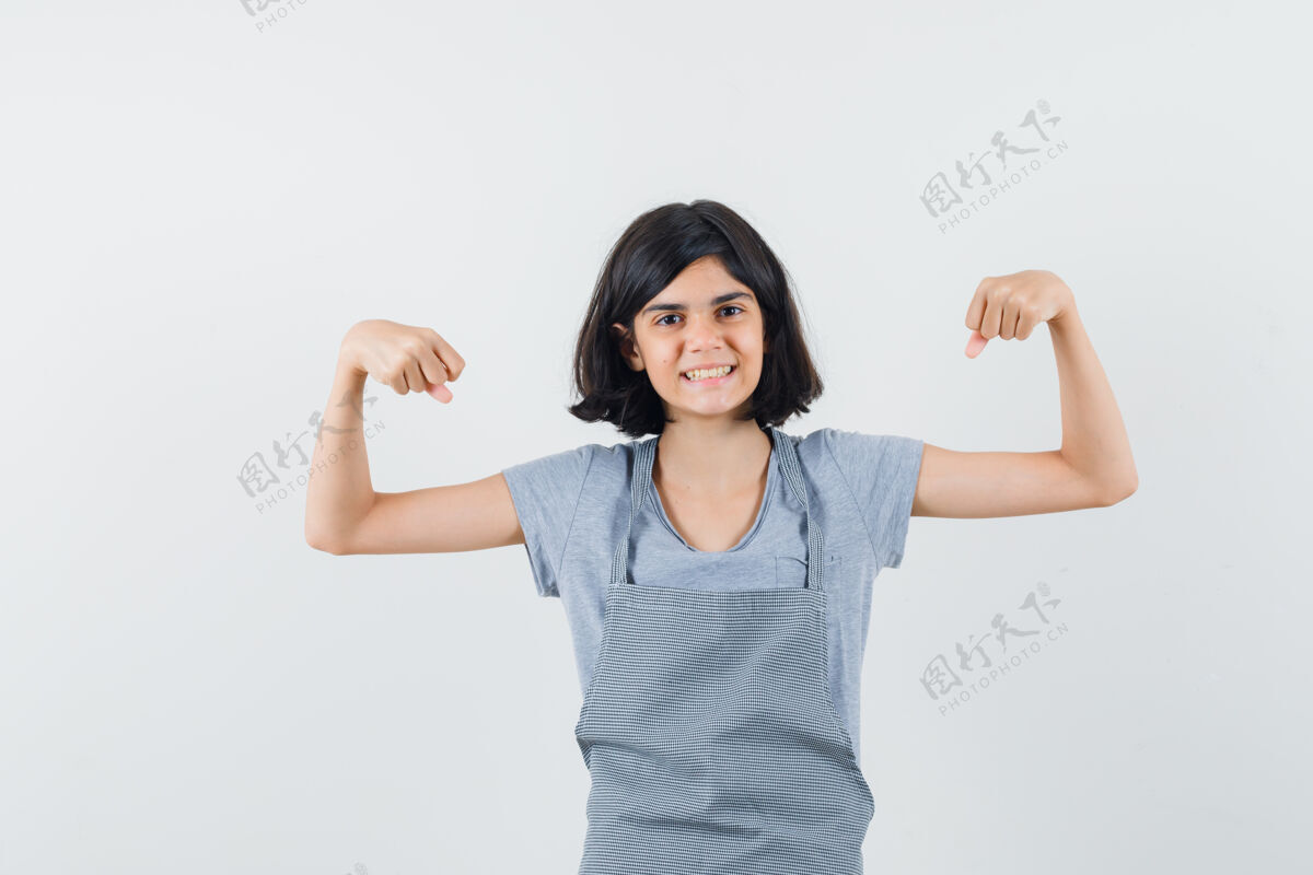 人小女孩在t恤 围裙显示肌肉的手臂和看起来自豪 前视图睡眠女孩脸