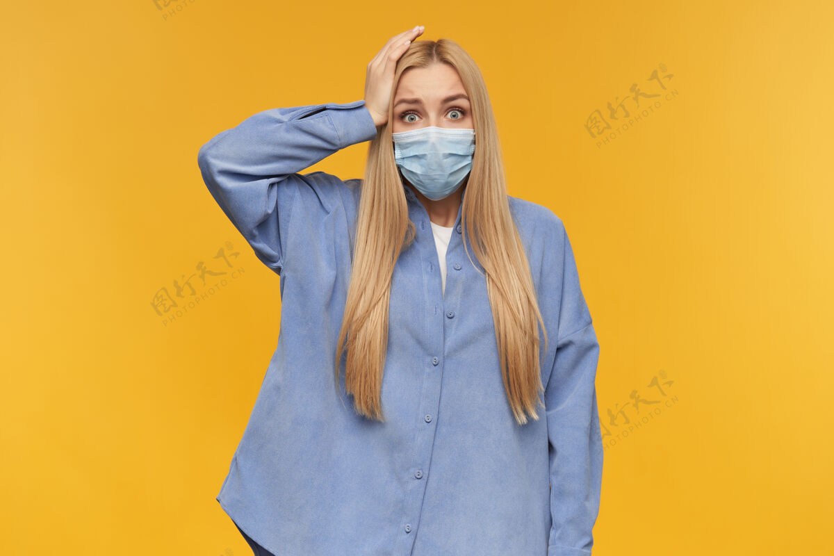 成人十几岁的女孩 一头金色长发的快乐女人 手放在头上 做着可怕的鬼脸穿着蓝色衬衫和医用面罩人和情感的概念自然服装防护