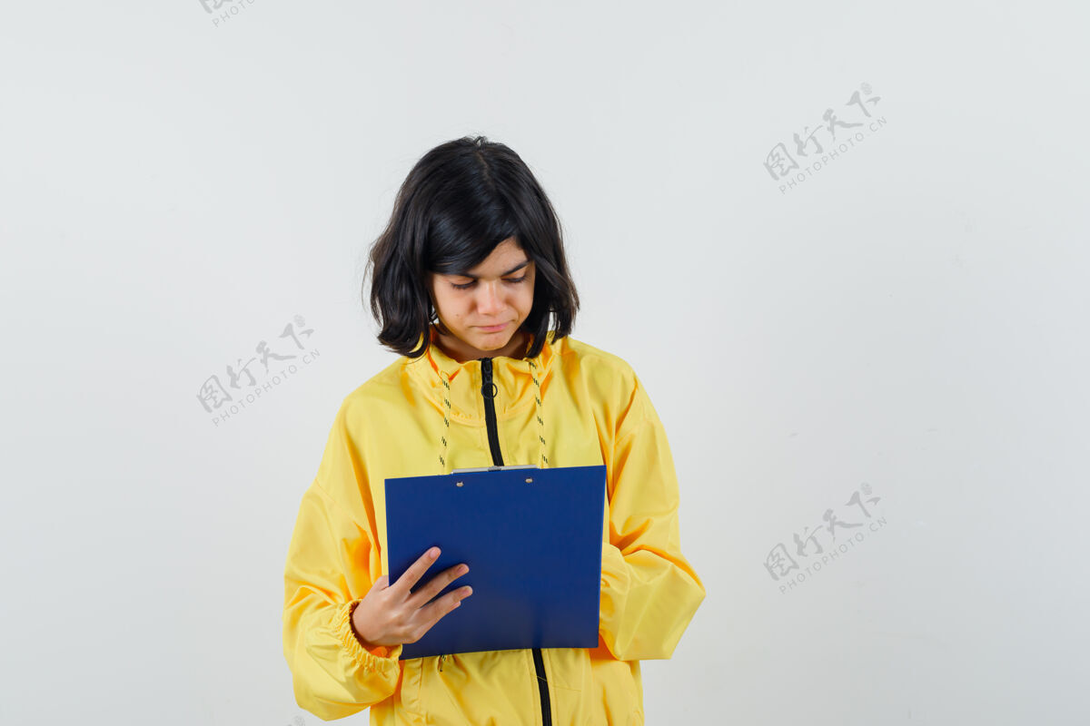 西班牙裔穿着黄色连帽衫的小女孩在剪贴板上做笔记 看起来很忙 正对着视图女孩休闲人