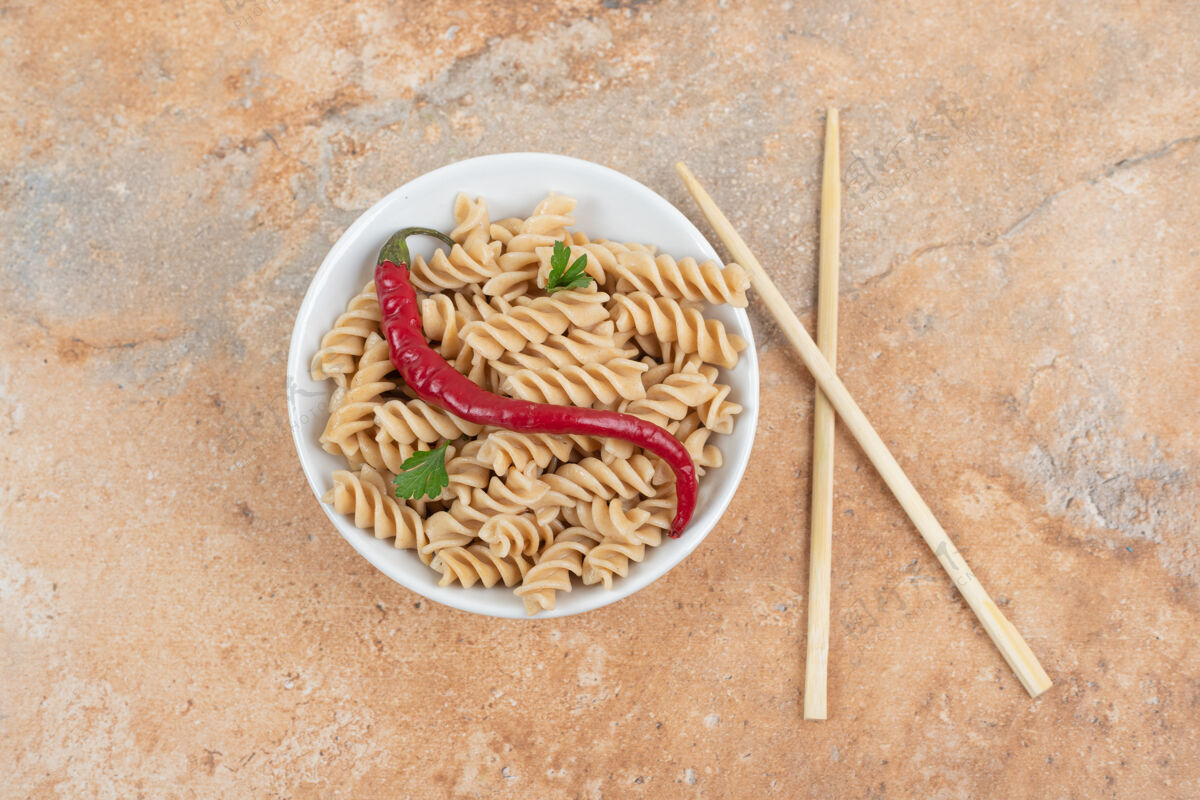 福西利大理石桌上放着一碗胡椒粉和筷子的意大利面高质量的照片辣椒欧芹碗
