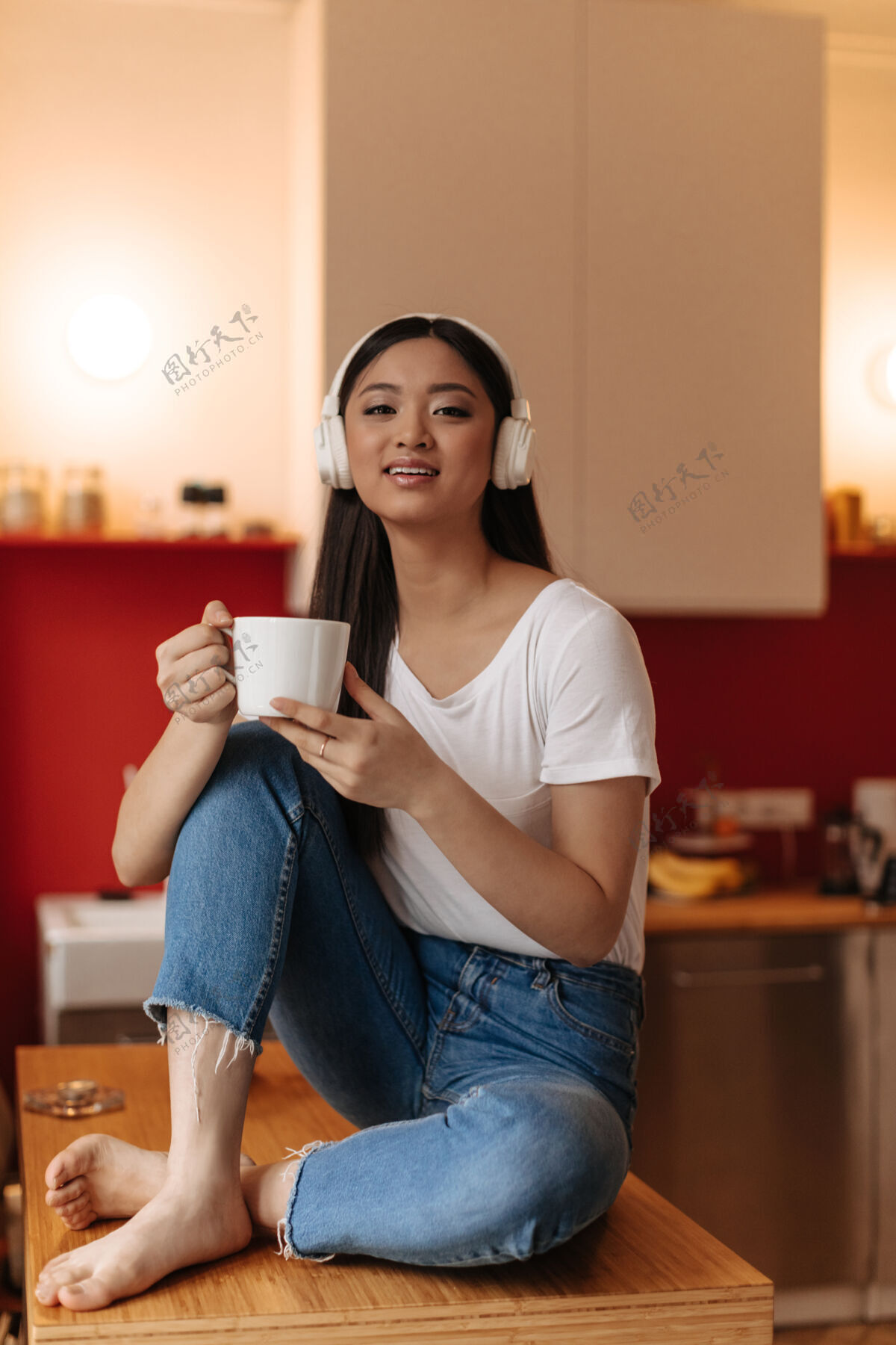 女人可爱的黑发女人戴着耳机坐在厨房里喝茶通信电话休闲