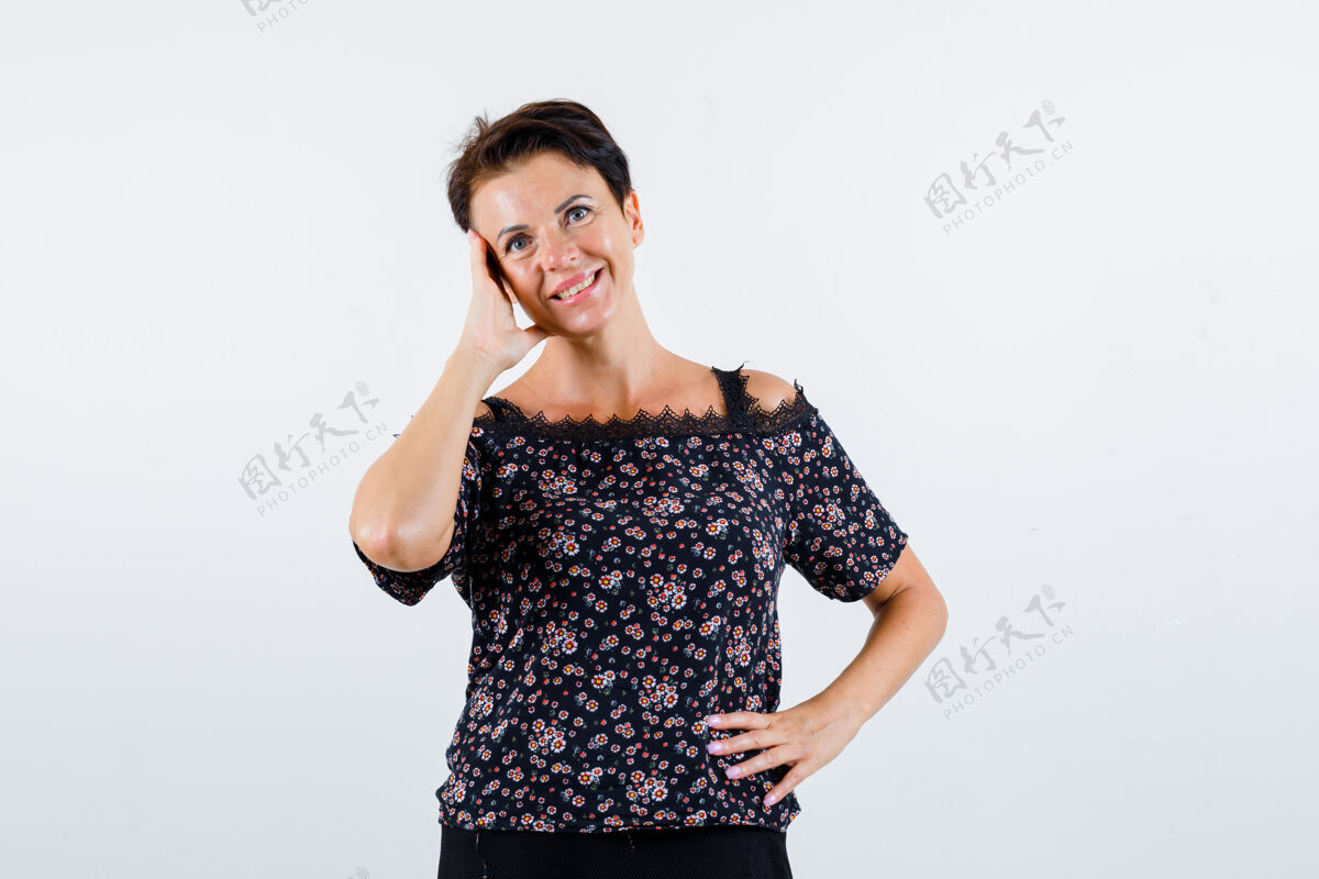 成人成熟的女人手放在腰上 面颊靠在手掌上 穿着花衬衫 黑色裙子 微笑着 看起来很开心正面图优雅女性健康