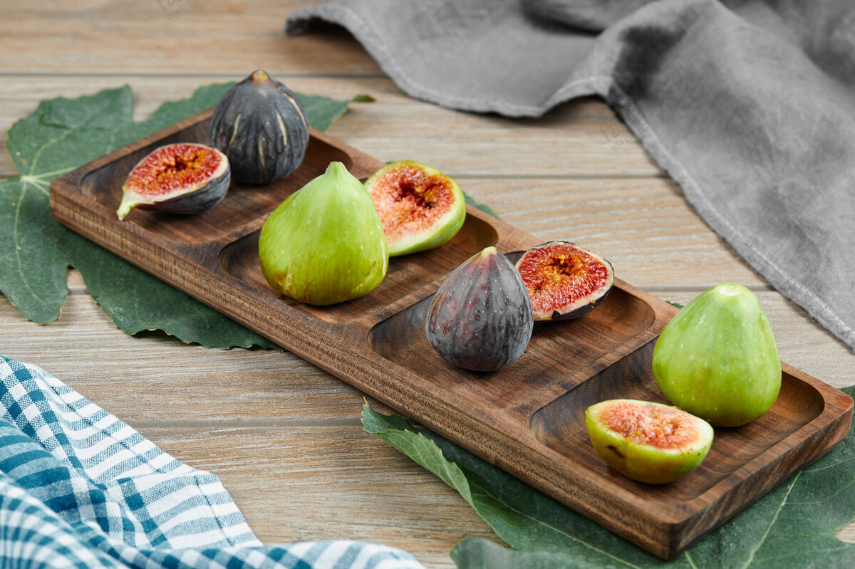 健康绿色和黑色的无花果放在一个木制盘子里 上面放着叶子和桌布高质量的照片营养盘子美味