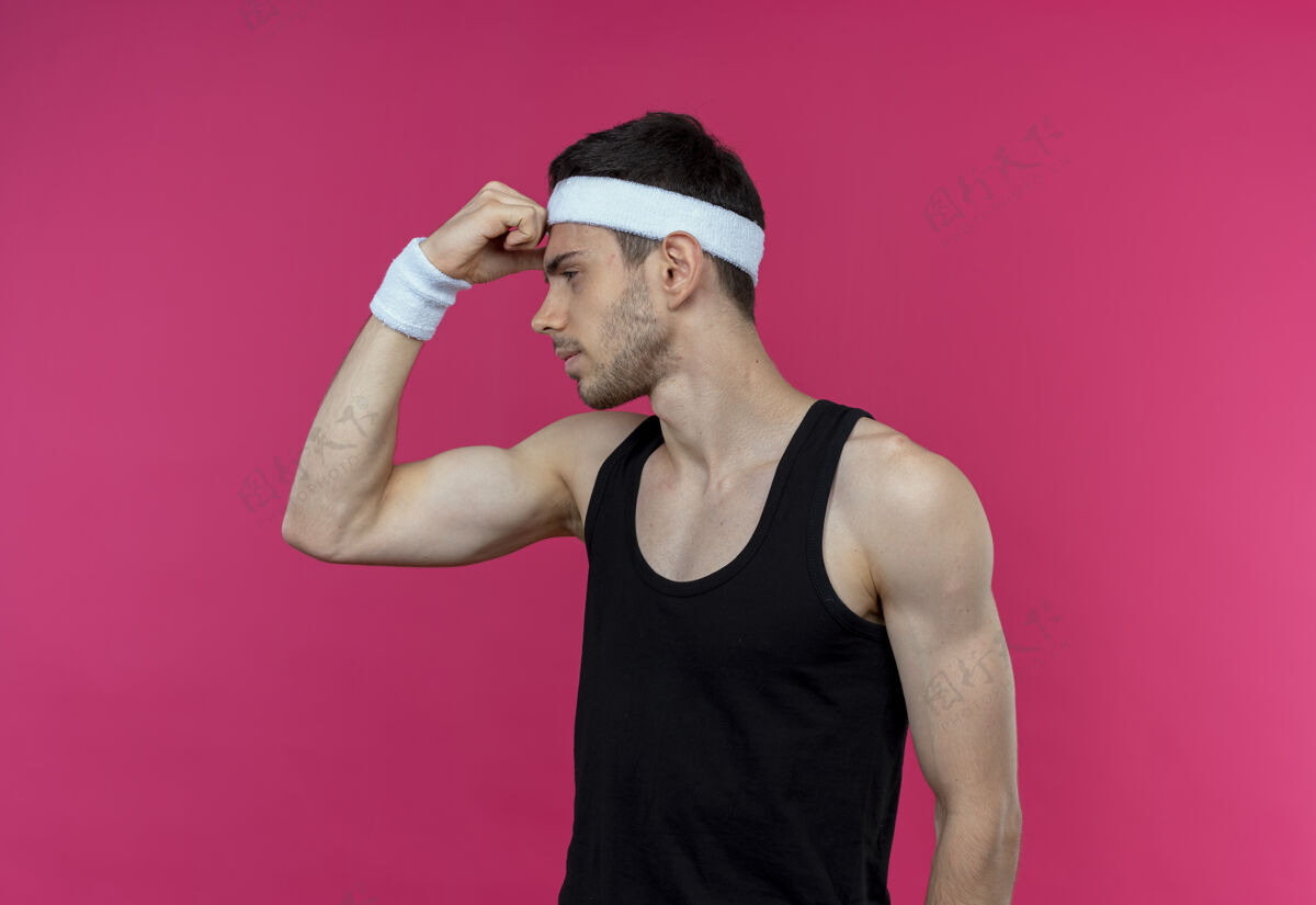 表情戴着头巾的年轻运动型男子站在粉色背景上 一边看一边露出自信的二头肌运动自信年轻