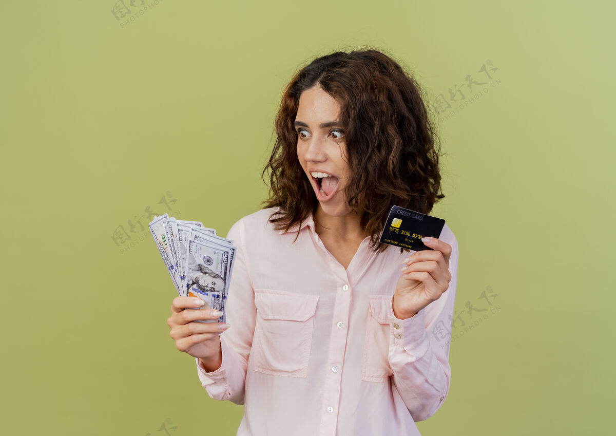 持有兴奋的年轻白人女孩拿着信用卡 看着绿色背景上的钱和复制空间隔离兴奋金钱女孩