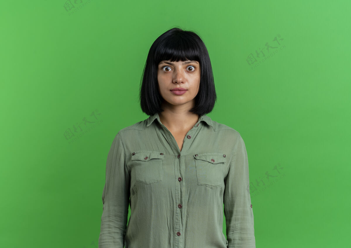 年轻震惊的年轻黑发高加索女孩看着相机在绿色背景与复制空间隔离黑发绿色复制