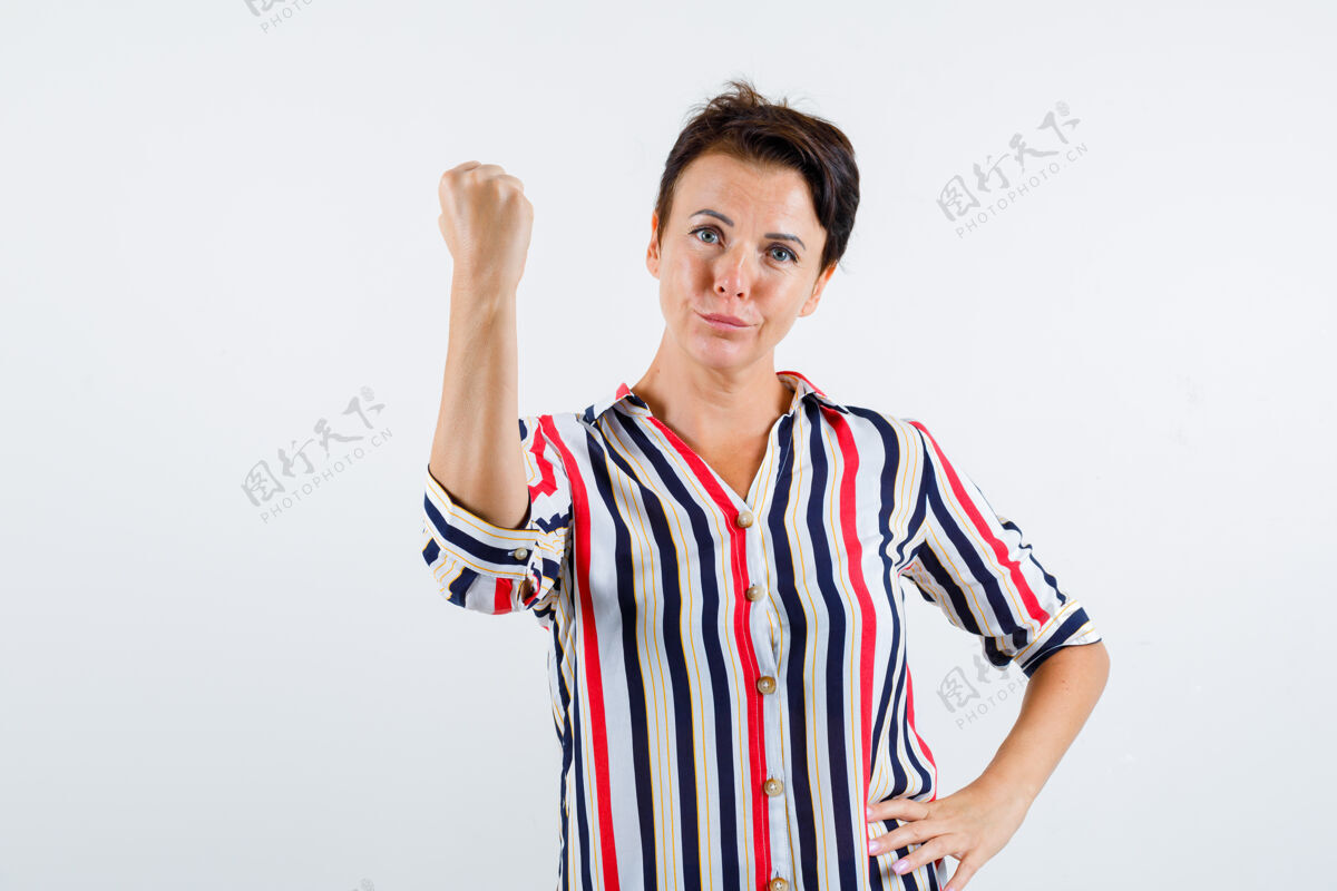 持有成熟的女人握紧拳头 手放在条纹衬衫的腰上 看起来很自信 前视优雅白发健身
