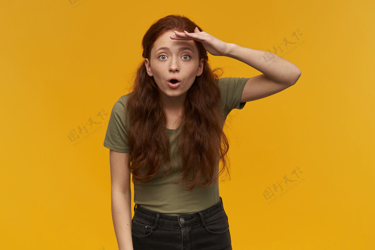 生姜惊讶 积极的女人 长着姜黄色的头发穿着绿色的t恤人和情感的概念用手掌遮住眼睛凝视远方被隔离在橙色的墙上脸表情情绪