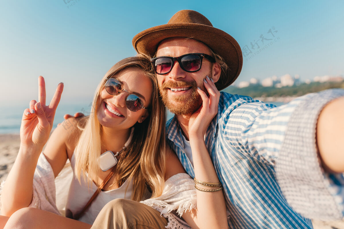 关系年轻迷人微笑戴墨镜的快乐男女坐在沙滩上自拍情人浪漫电话