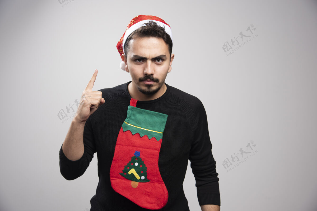 乐观一个戴着圣诞老人帽子的年轻人拿着圣诞袜子竖起手指手和平T恤