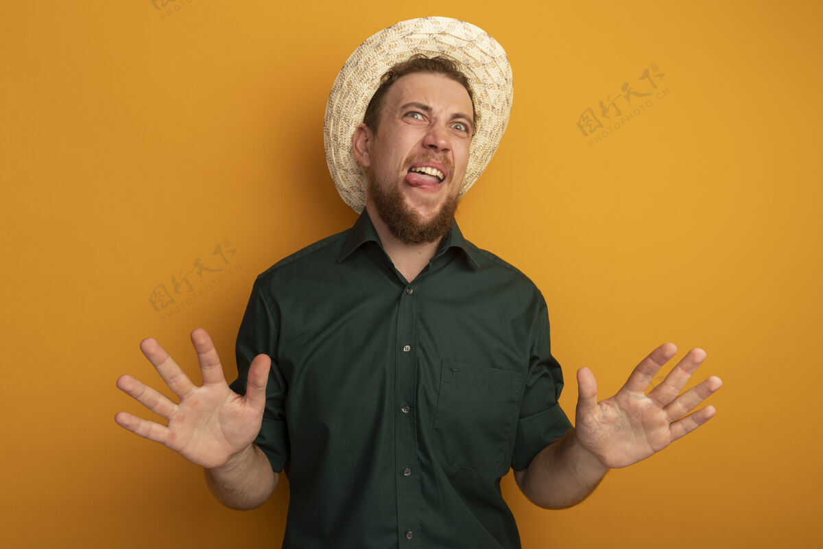 姿势一个戴着沙滩帽的金发帅哥在橘色的墙上张大了嘴 张开了双手人衣服不愉快