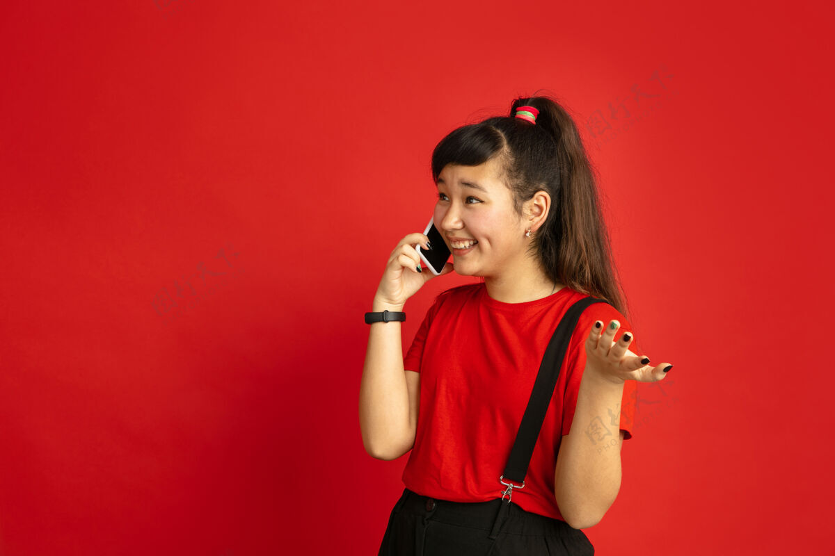 手势在红色工作室背景上孤立的亚洲青少年肖像美丽的深褐色女性模特 随意的长发人类情感的概念 面部表情 销售 广告电话交谈人年轻人女孩