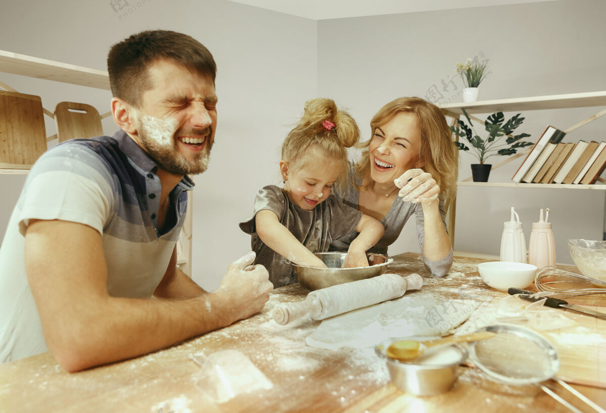 积极可爱的小女孩和她美丽的父母在家里的厨房里准备蛋糕家庭生活方式的概念微笑晚餐夫妇