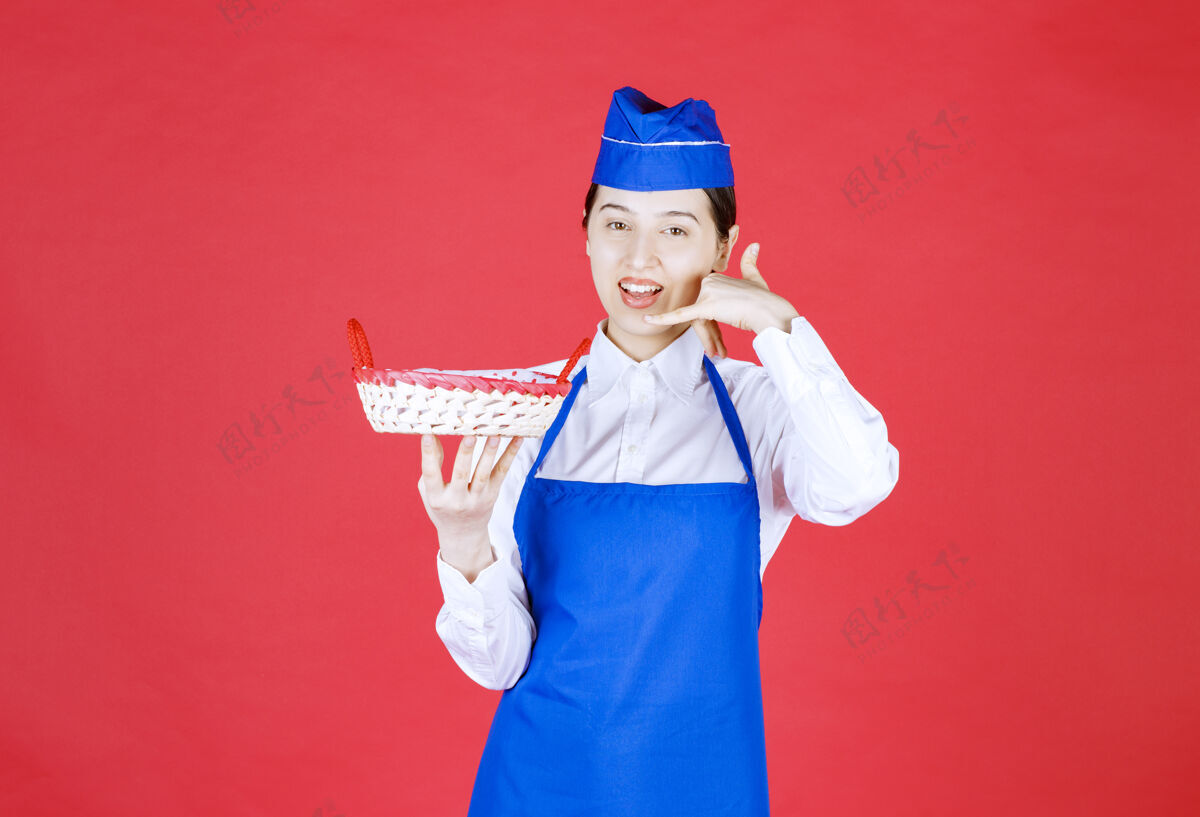 人穿着蓝色围裙的面包师手里拿着一个面包篮 里面放着红毛巾 要求打电话点菜服装员工人
