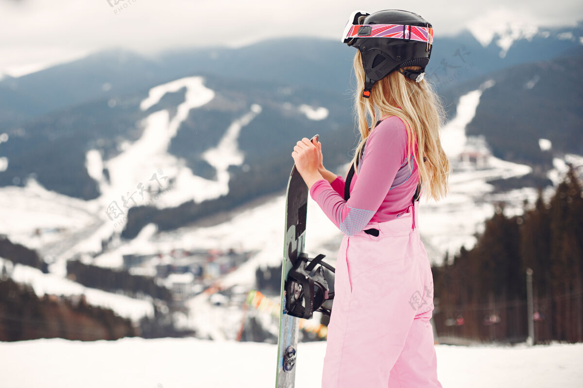一个穿着滑雪板套装的女人在山上手拿滑雪板的运动员在地平线上关于运动的概念运动活跃粉色