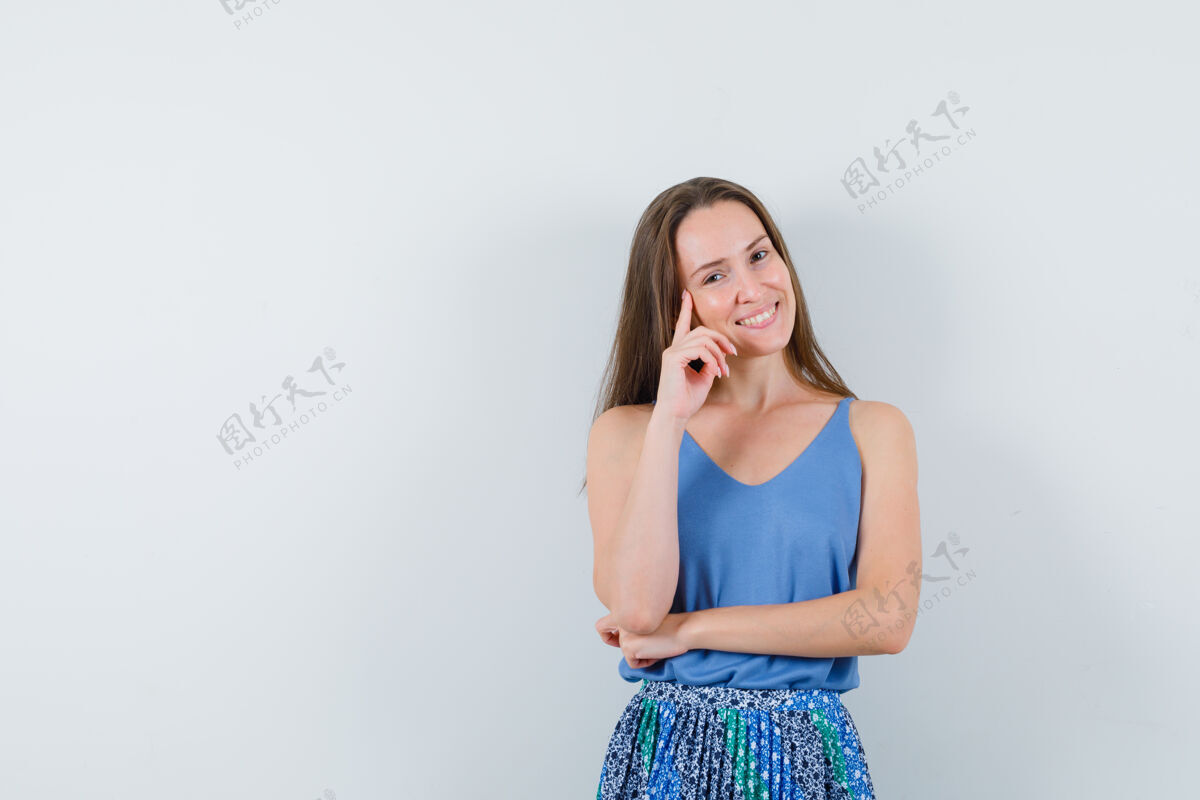头发年轻的女士站在思考的姿势在单打 裙子和看起来愉快 前视图微笑单身完美