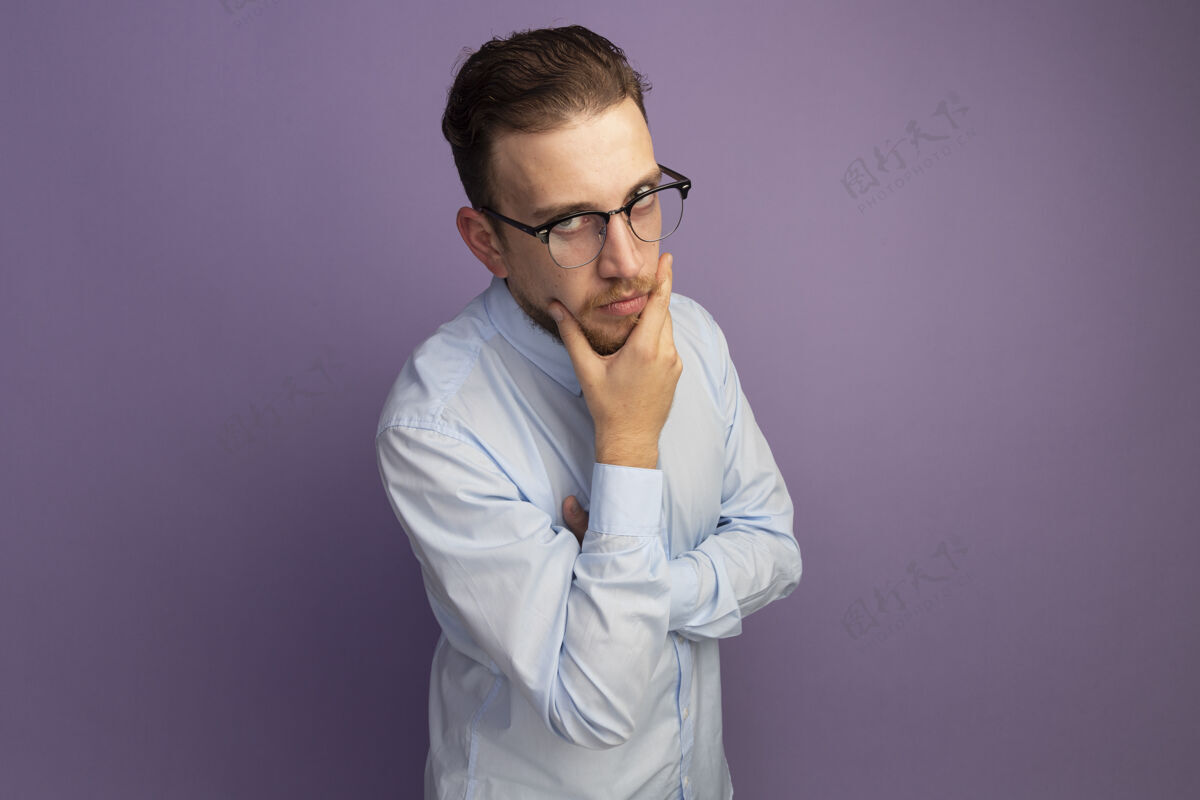 人自信的金发帅哥 戴着眼镜 托着下巴 看着隔离在紫色墙上的前面市民站着抱着