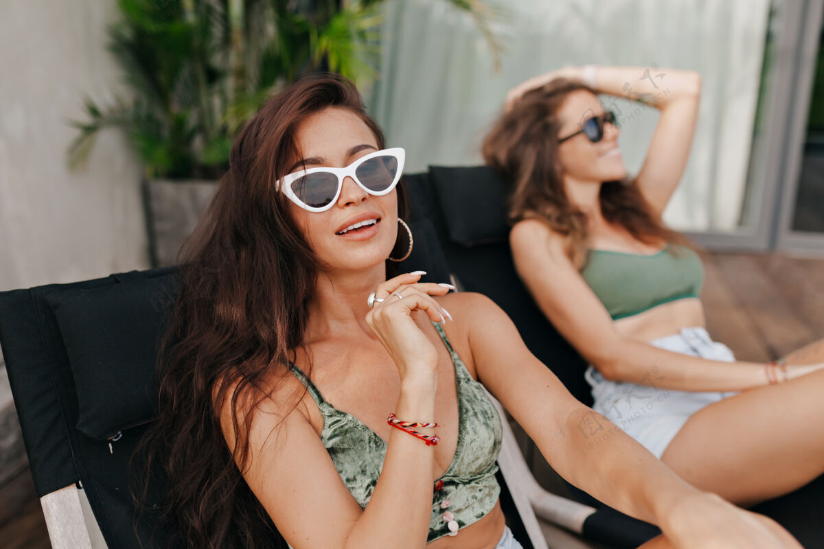 热在阳光明媚的日子里 两位美丽的女性朋友在日光躺椅上玩耍和休息的户外写真性感游泳池边皮肤