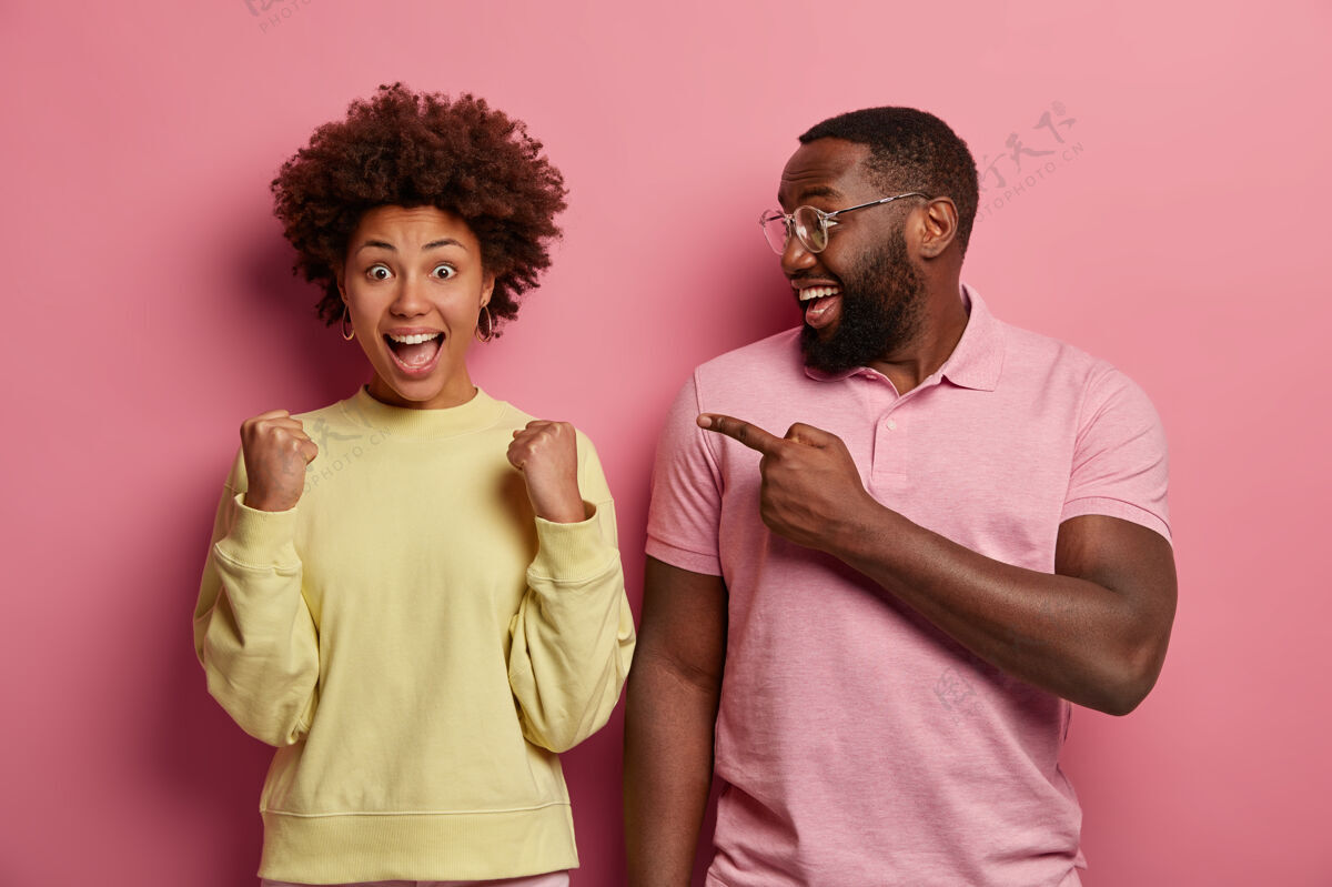 美国人快乐的黑胡子男人紧握拳头指着胜利的女人 庆祝成功 高兴地大叫 表达积极的情绪看女性指示器非洲人