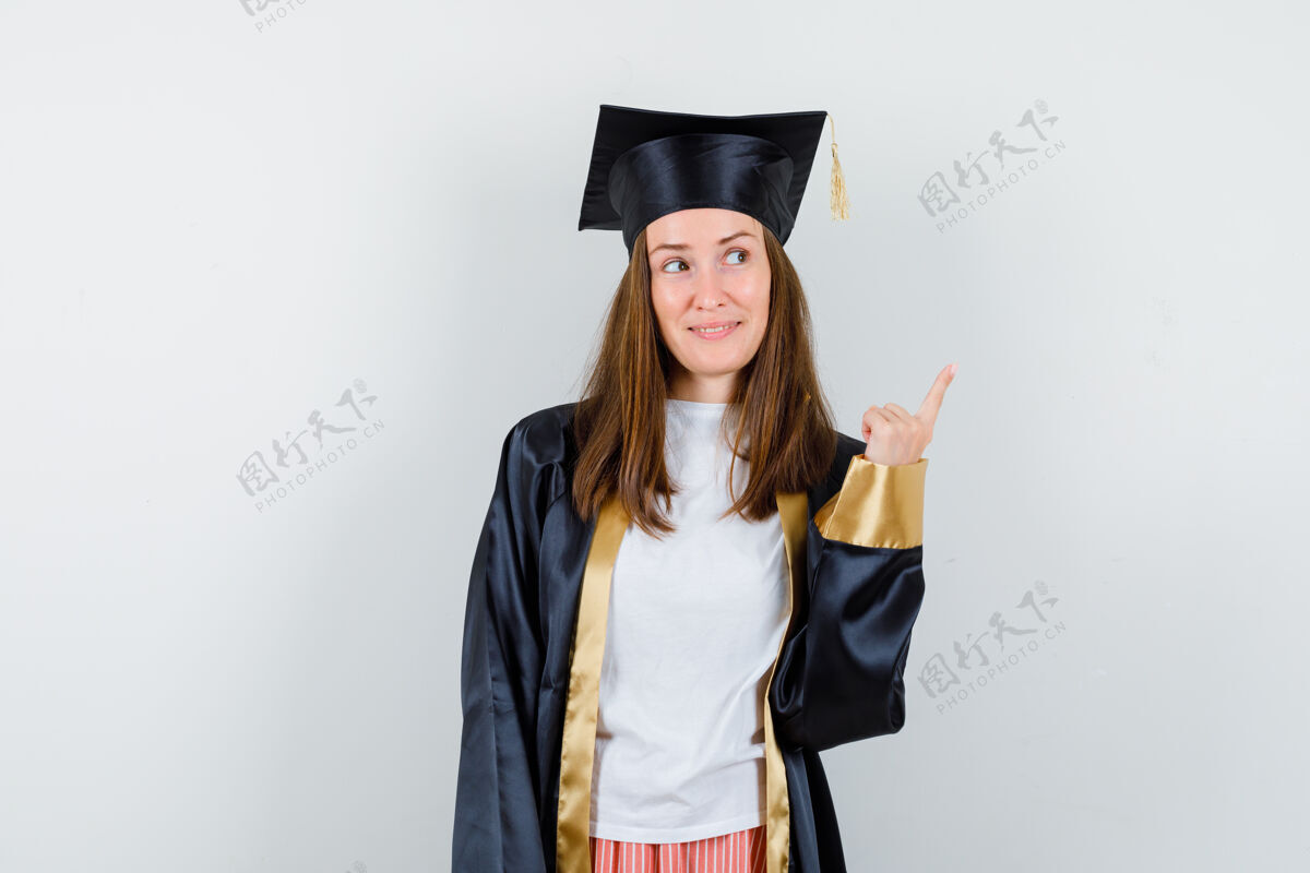 微笑身着学院服的女毕业生指着右上角 看上去充满希望 前视图学校长袍成人
