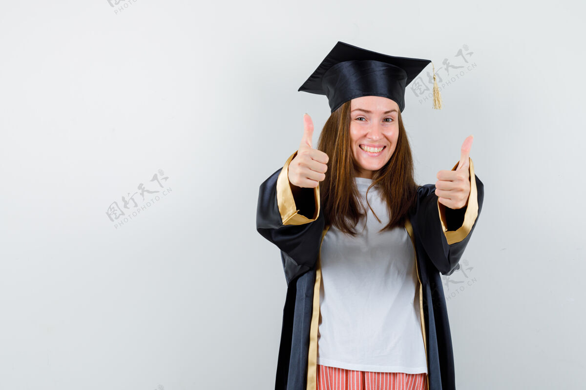 年轻毕业妇女的肖像显示双拇指在休闲服 制服 并期待幸福的前视图人学位休闲