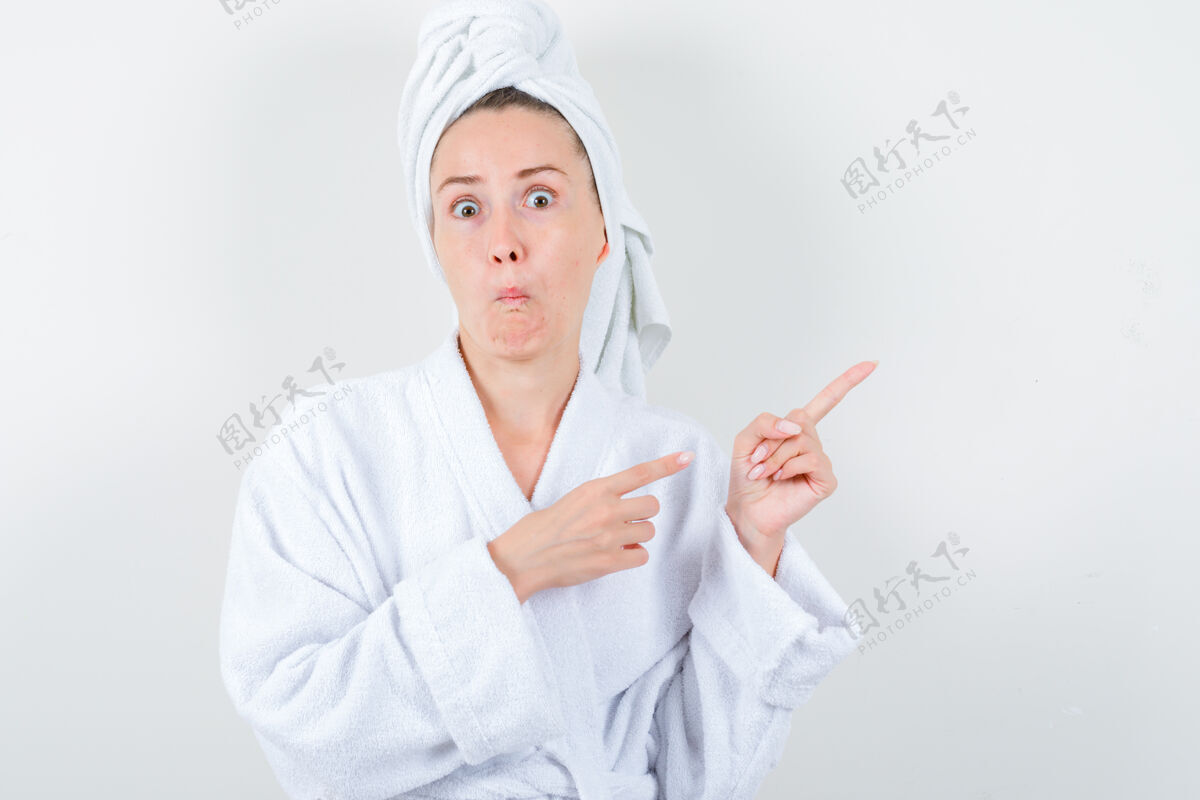 右年轻女士指着右上角的白色浴衣 毛巾和期待惊讶前视图指健康肖像