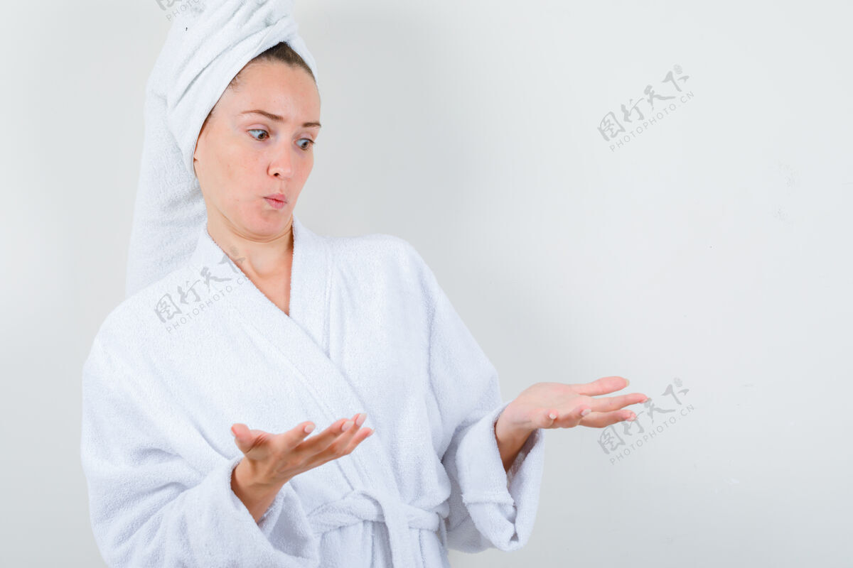 自然穿着白色浴袍的年轻女士 用毛巾欢迎着什么东西 看上去很困惑 前视图东西黑发漂亮
