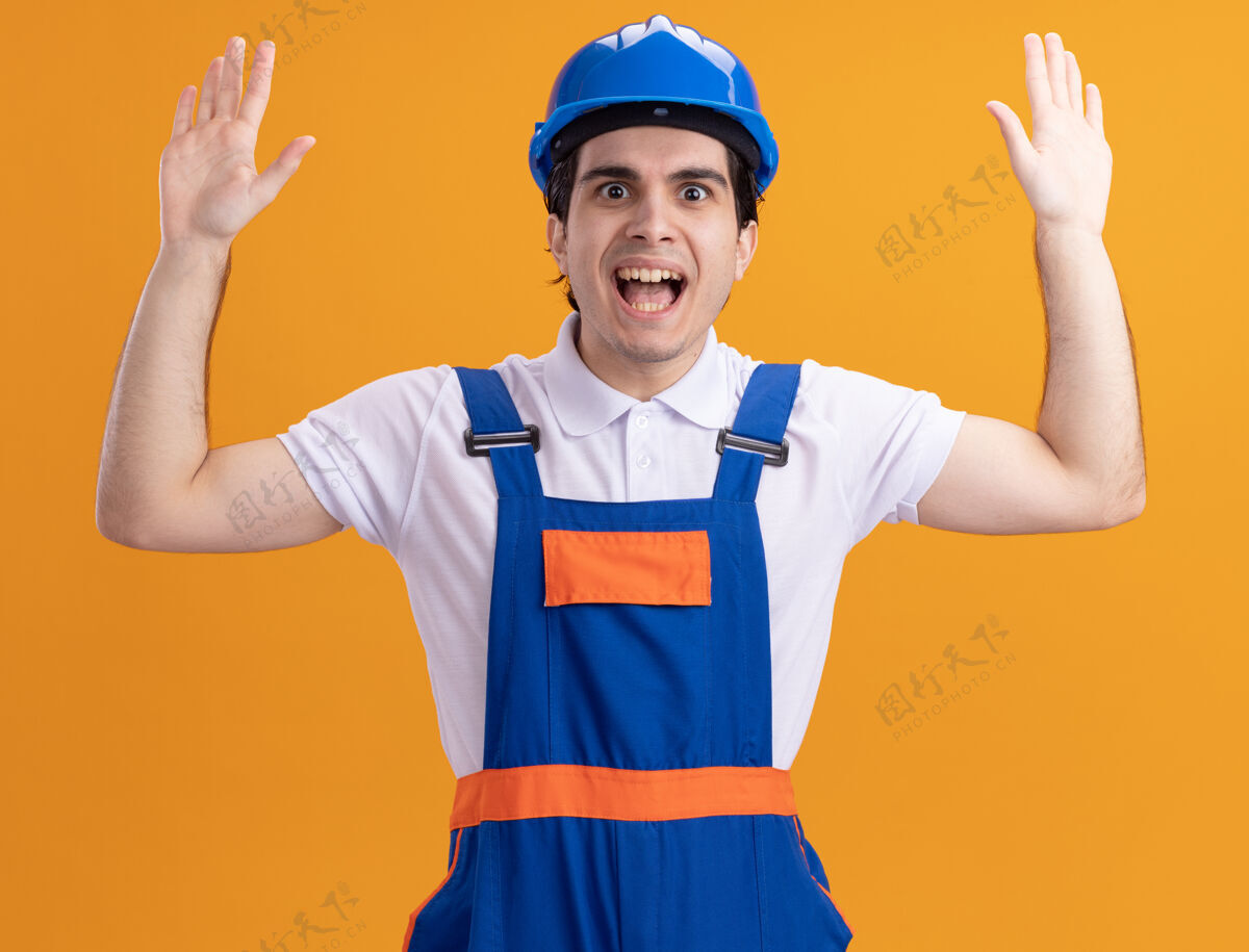 建筑年轻的建筑工人穿着建筑制服 戴着安全帽 站在橘色的墙上 惊讶地抬起手掌望着前面安全手掌男人