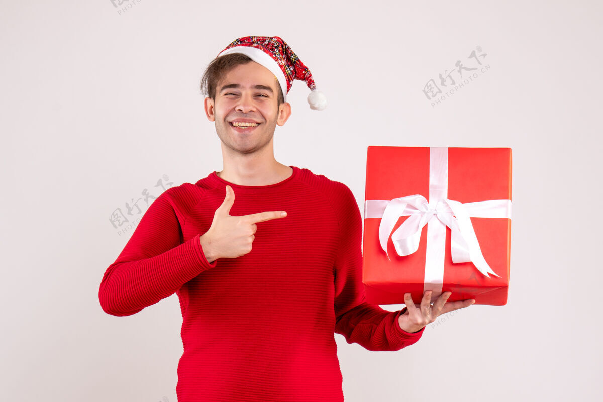 圣诞节前视图：戴圣诞帽的年轻人指着白色背景上的礼物欢呼圣诞老人乐趣