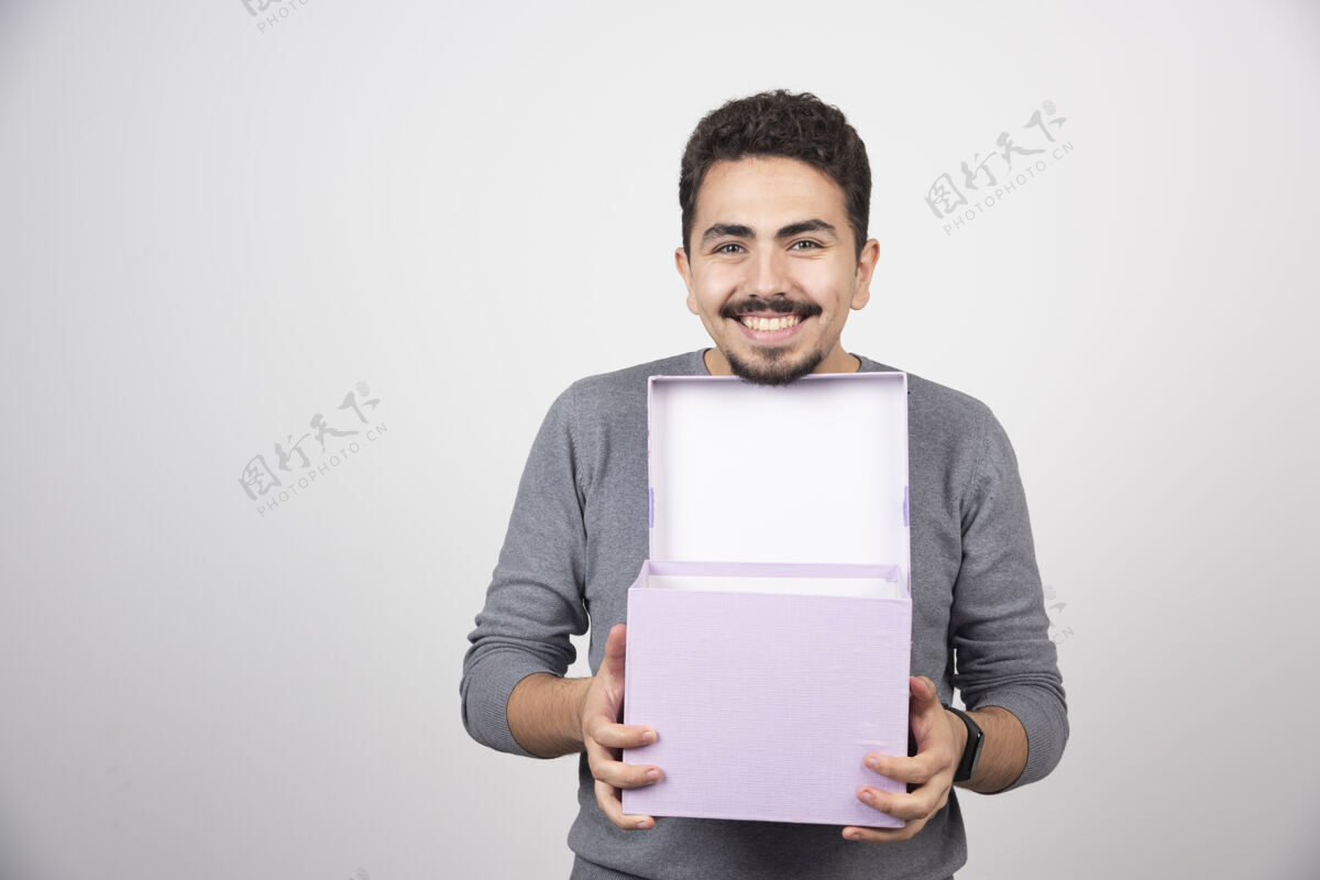 男孩带着微笑的男人 在白色的墙上放着一个打开的紫色盒子模特紫色人