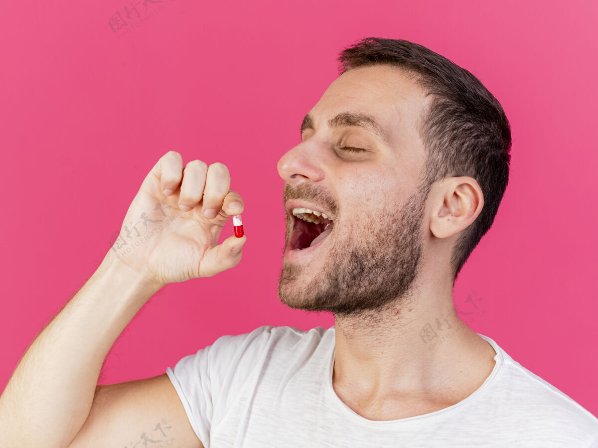 眼睛年轻的病人闭着眼睛 把药片放进嘴里 隔离在粉红色的背景上药丸疾病嘴巴
