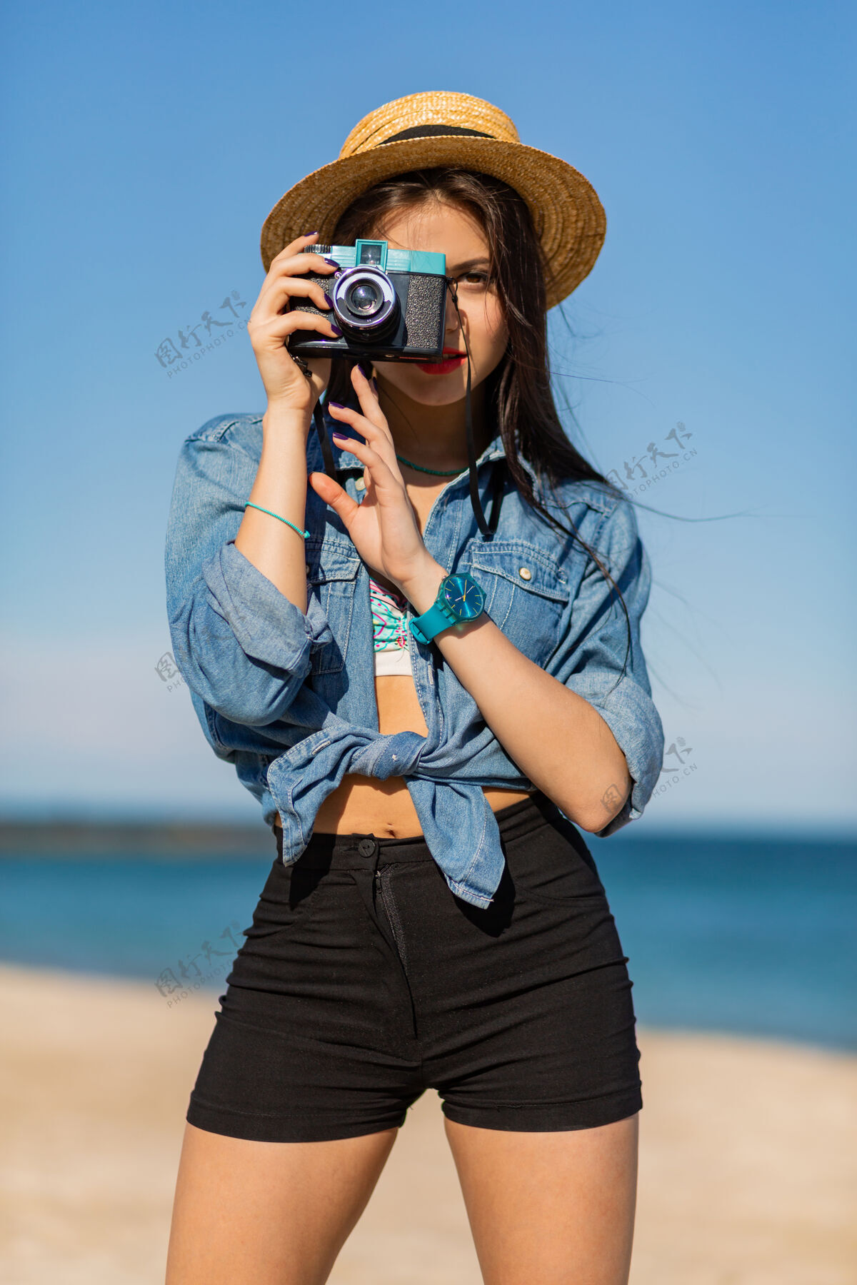 魅力棕褐色身材 红唇丰满 长腿的女人在热带阳光明媚的海滩上摆姿势穿着短上衣 短裤和草帽年轻热带女性