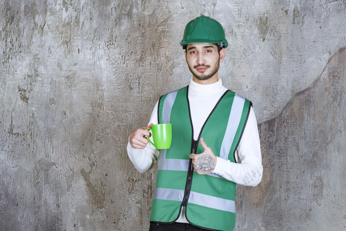 交易身着黄色制服 头戴安全帽的工程师手拿着一个绿色的咖啡杯 享受着产品精力充沛工人喜欢
