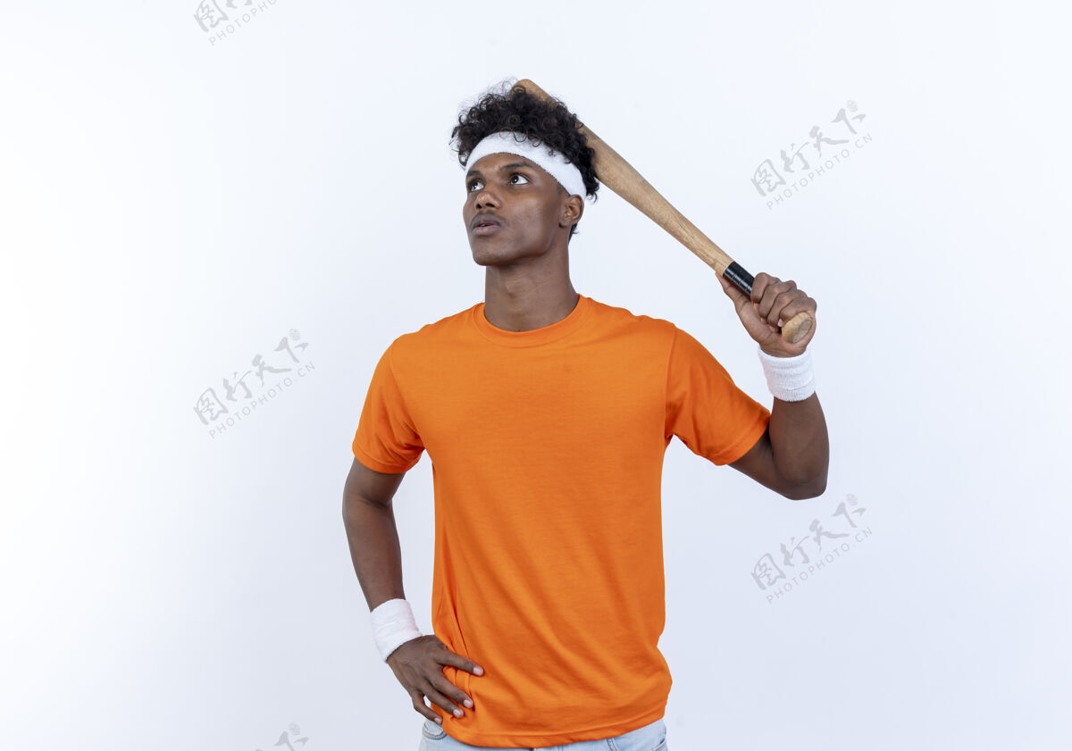 头看着身边年轻的美国黑人运动男子戴着头带和腕带拿着蝙蝠在头上 把手放在臀部隔离在白色背景腕带手运动型
