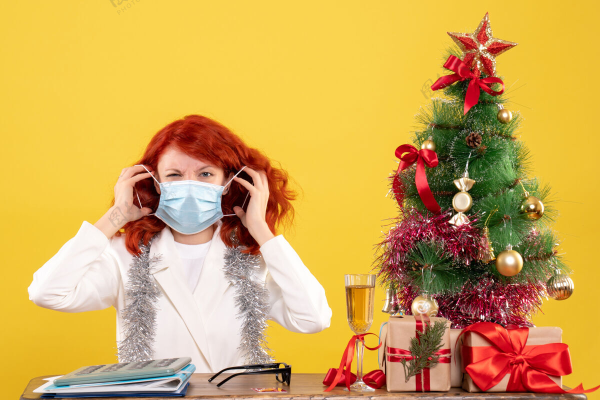 病毒前视图女医生围绕圣诞树和礼物坐在面具面具树圣诞