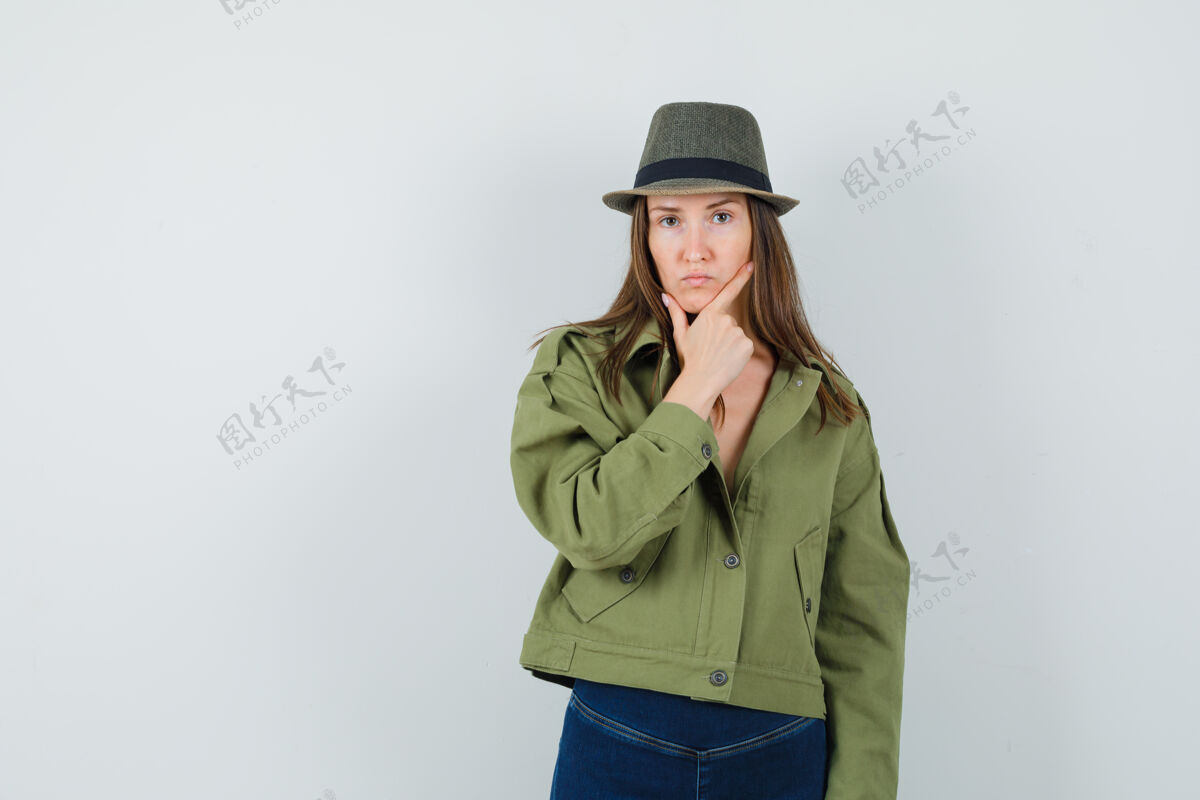 人类年轻的女士站在思考的姿势在夹克裤子帽子 看起来很严肃连衣裙休闲严肃