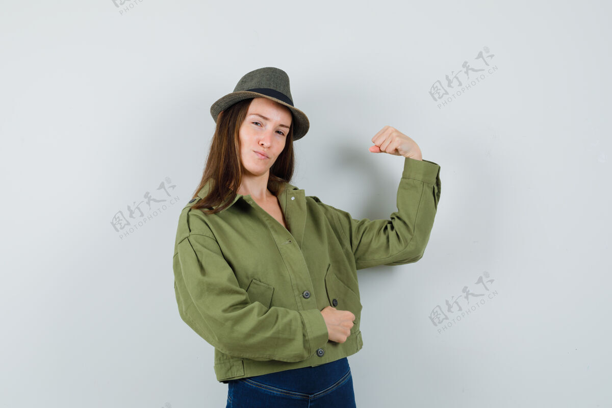 裤子穿着夹克 裤子 帽子 展示手臂肌肉的年轻女士 看起来很自信时尚夹克优雅