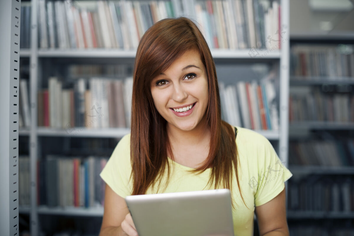 研究快乐的学生在图书馆使用数字平板电脑书架欢呼年轻的女人