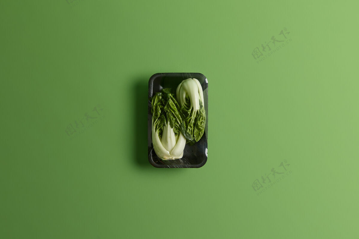 美食黑色托盘上用保鲜膜包裹的白菜或白菜绿色背景下超市出售的新鲜蔬菜健康的生活方式 茶点和营养理念生的膳食新鲜