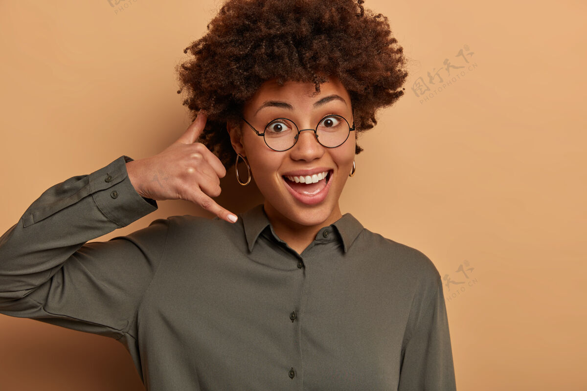 手指你好 我听到了高兴的女人模仿电话 在耳边做移动手势 开心地微笑 享受远距离交流 穿着深色衬衫 戴着透明眼镜正面通话展示