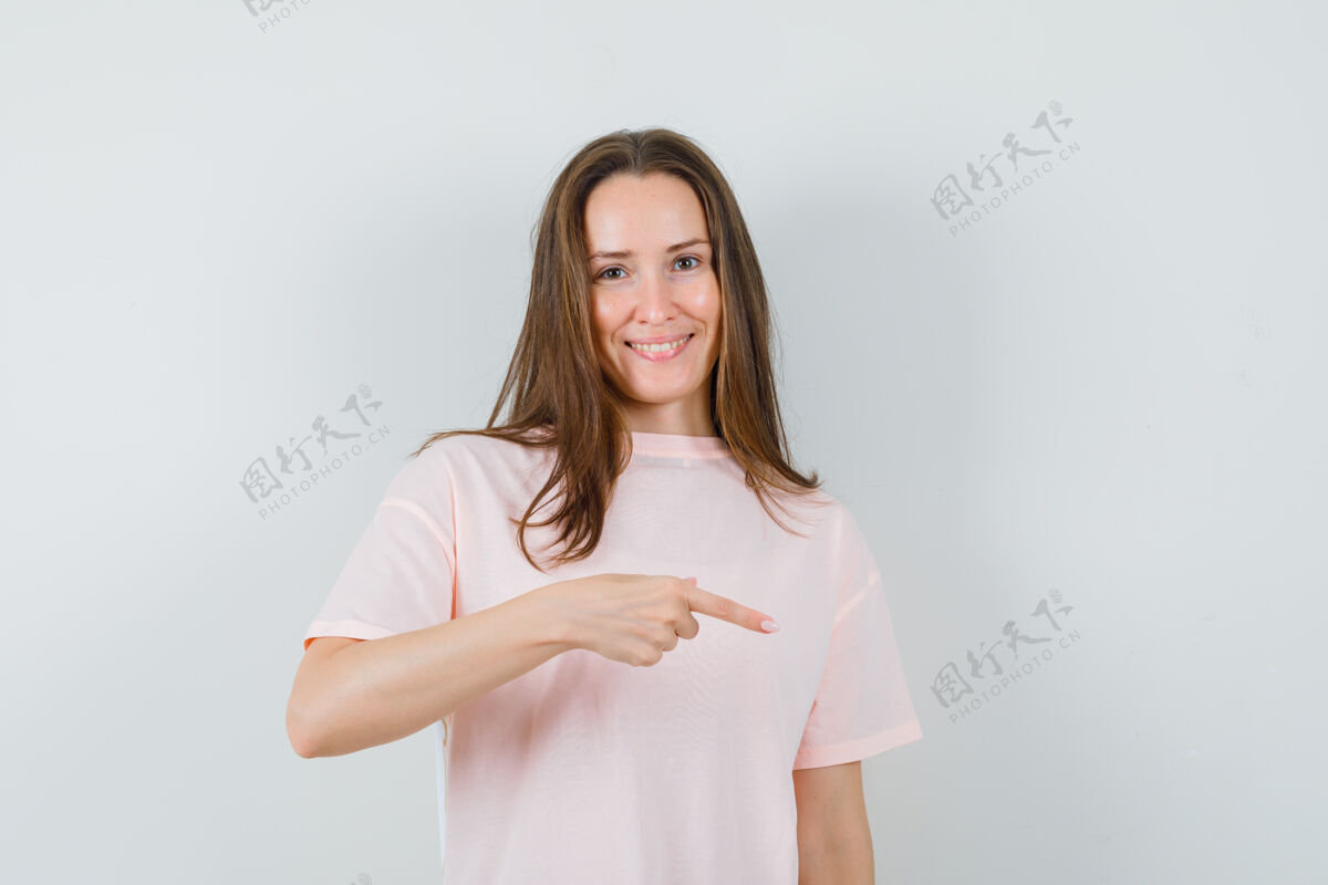 快乐穿着粉色t恤的年轻女士手指朝下 看起来很高兴指向一起积极