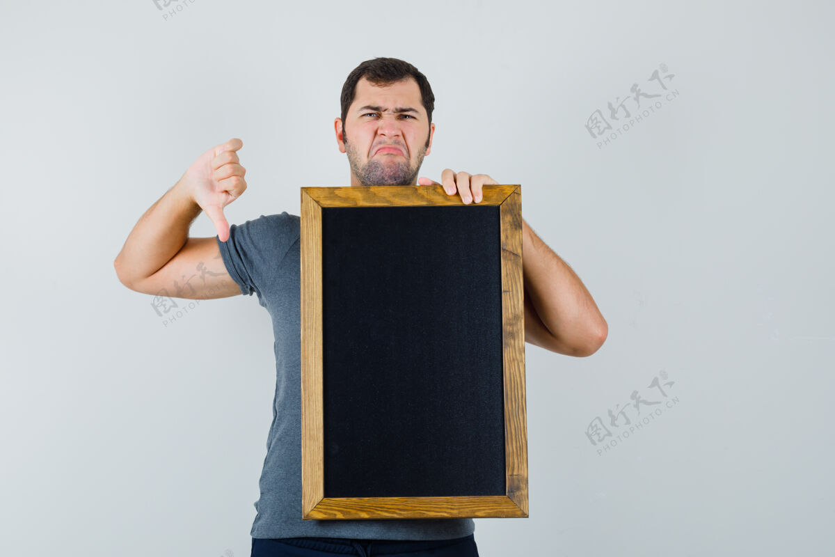 现代年轻人拿着黑板 穿着灰色t恤 拇指朝下 看上去很不满黑板抱胡须
