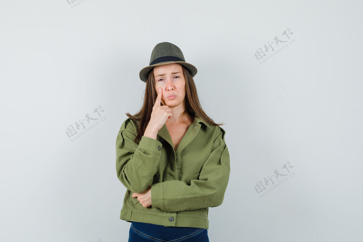 夹克穿着夹克 裤子 帽子 手指贴在脸颊上的年轻女士看起来很沮丧休闲举行黑发