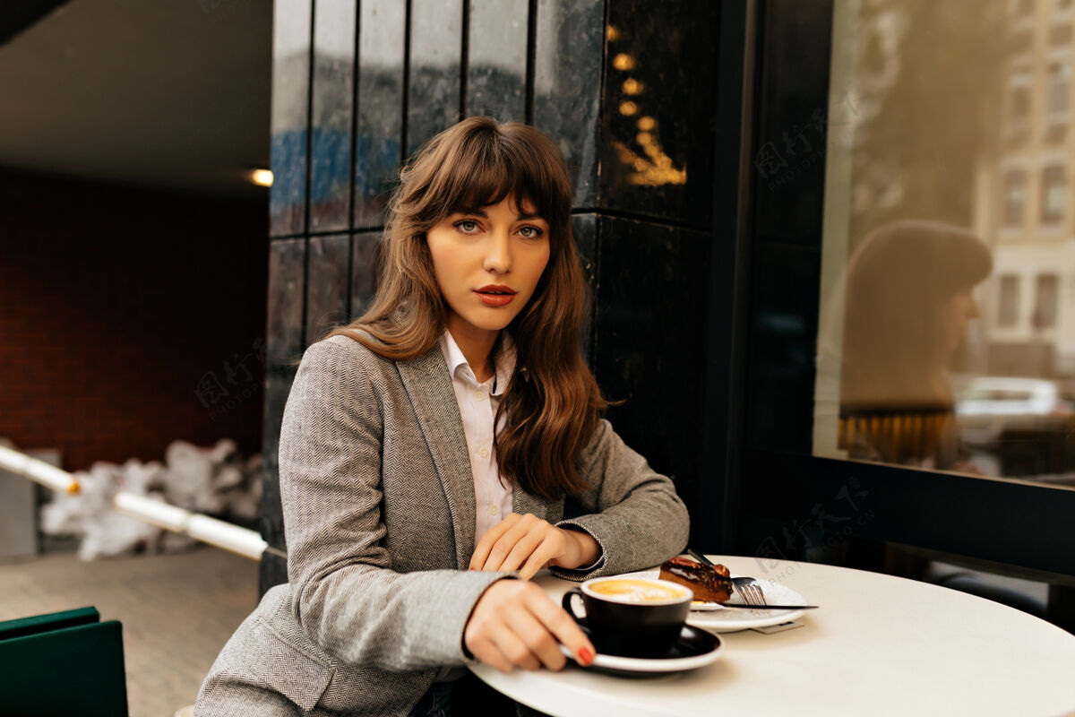 商业女性一位穿着灰色夹克 留着波浪长发的迷人女士坐在城市自助餐厅里 正在喝咖啡搜索女士集中