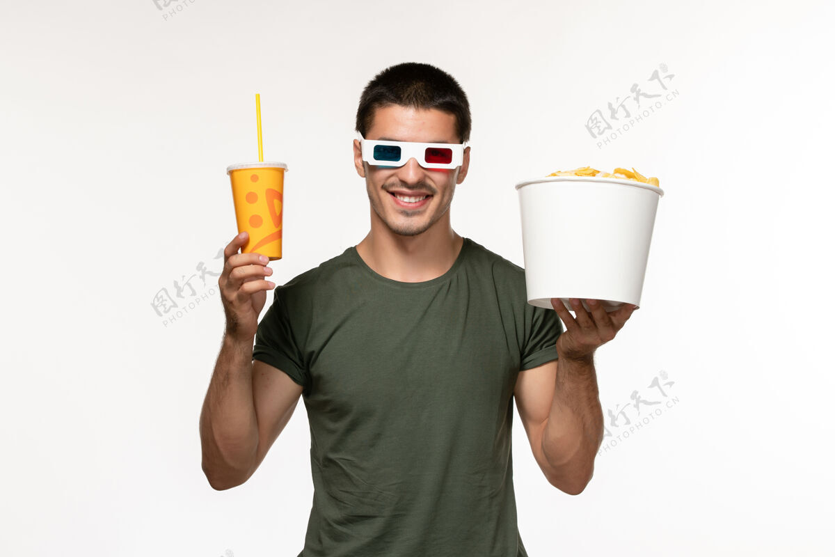 年轻男性正面图身穿绿色t恤的年轻男性手持马铃薯cips苏打水戴着d太阳镜在白墙上拍摄电影男性孤独电影电影院苏打水电影土豆